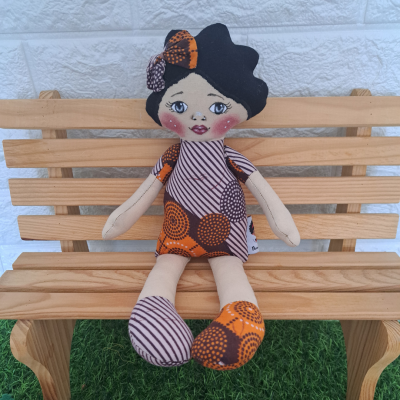 Boneca de tecido com roupa laranja e roxa sentada num banco de madeira