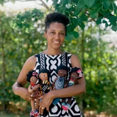 Mulher com vestido preto e branco segura quatro bonecas de tecido coloridas ao ar livre