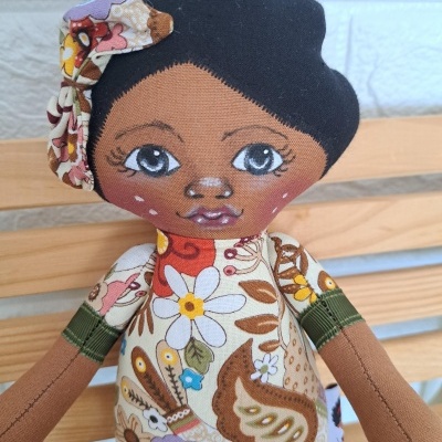 Boneca de tecido com vestido floral colorido e cabelo preto.
