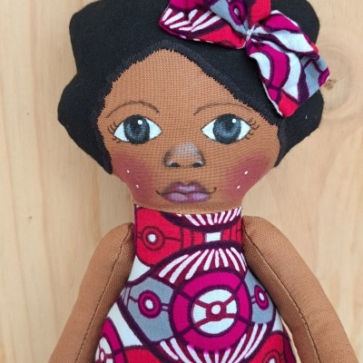 Boneca de pano com vestido vermelho e laço no cabelo sentada