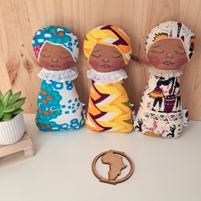 Três bonecas de pano com turbantes coloridos e gola branca, em fundo madeira clara