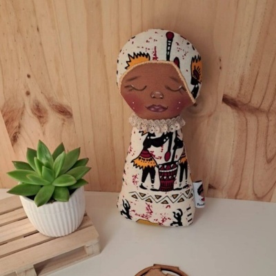 Boneca de tecido com padrão tribal e vaso com suculenta em fundo de madeira.