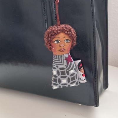 Brinquedo ou chaveiro em bolsa preta com rosto desenhado e cabelo encaracolado