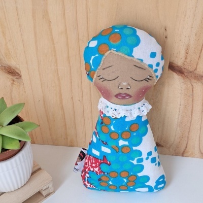 Boneco de pano com rosto pintado e tecido estampado colorido ao lado de planta em vaso branco