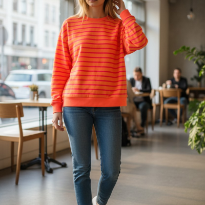 Mulher com camisola laranja às riscas vermelhas e jeans num café interior