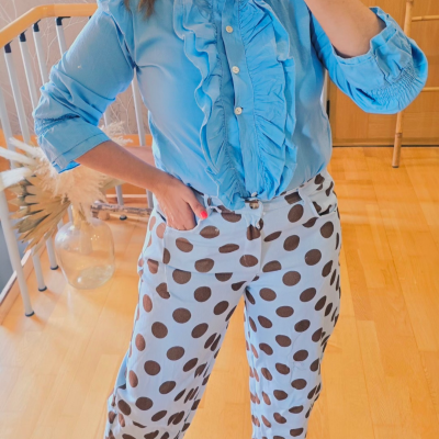 Pessoa a usar camisa azul com folhos e calças azul claro com bolinhas castanhas em interior