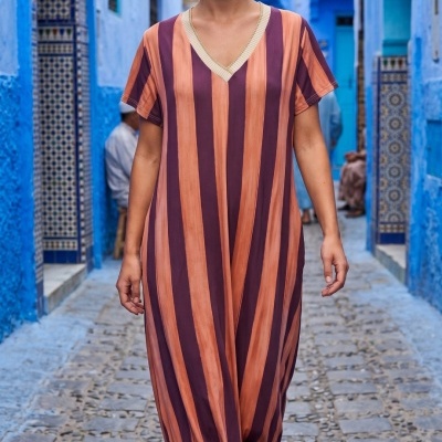 Vestido comprido às riscas laranja e roxo com decote em V em rua com paredes azuis e pavimento de pedras.