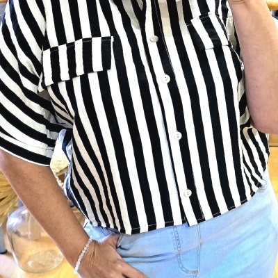 Camisa às riscas verticais preto e branco com botões e bolsos no peito, usada com jeans azul claro.