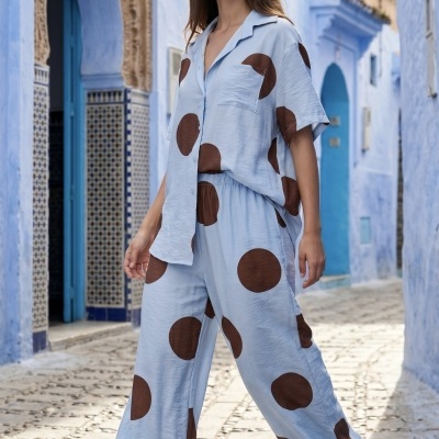 Mulher a usar conjunto azul claro com bolinhas castanhas grandes, em rua com paredes azuis.
