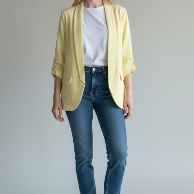 Mulher com blusão amarelo claro, t-shirt branca, jeans azuis e ténis brancos em fundo cinza claro