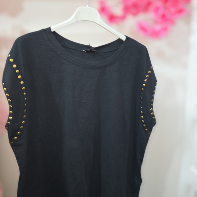 T-shirt preta com tachas douradas nas mangas pendurada num cabide branco