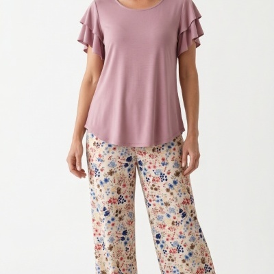 Mulher com t-shirt rosa e calças largas florais em fundo branco.