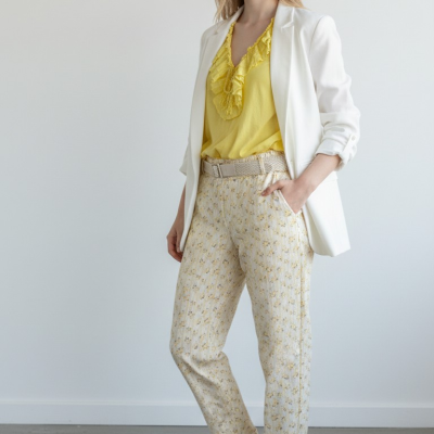 Mulher com blazer branco, blusa amarela, calças florais e ténis brancos em fundo branco