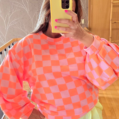 Pessoa vestindo sweatshirt xadrez rosa e laranja fluorescente e calças amarelas claras em ambiente interior