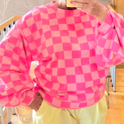 Sweatshirt rosa com padrão quadriculado e calças amarelas, ambiente interior doméstico.