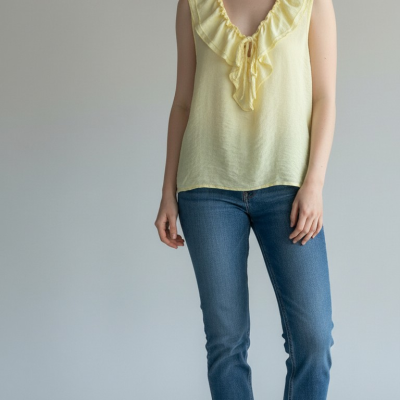 Mulher com top amarelo claro sem mangas, jeans azul e ténis brancos