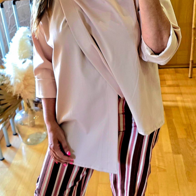 Blusa bege com gola alta e botão e calças largas às riscas verticais castanhas, brancas e vermelhas em chão de madeira clara