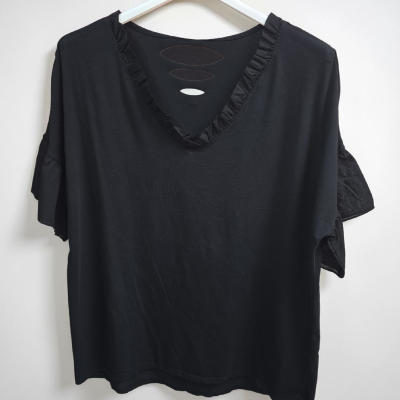 T-shirt preta com decote em V e folhos pendurada num cabide branco