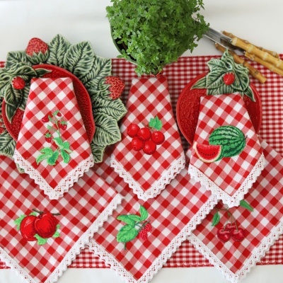 Guardanapos vermelhos e brancos com bordados de frutas e pratos de cerâmica com folhas e morangos