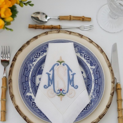 Conjunto de talheres com cabos de bambu e pratos decorados com guardanapo monogramado numa mesa branca
