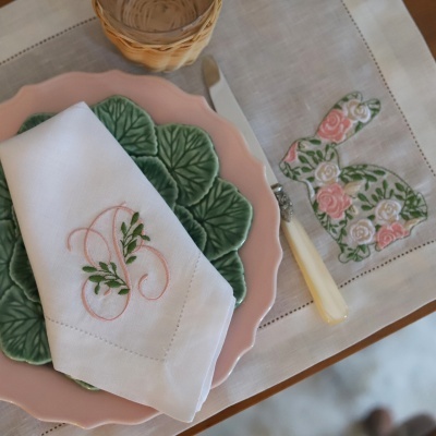Mesa posta com guardanapo branco bordado, pratos verde e rosa, faca e toalha bordada com coelho