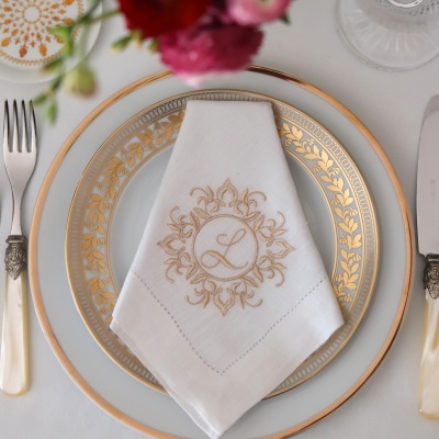 Conjunto de pratos brancos com decoração dourada e guardanapo bordado com a letra L