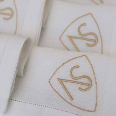 Toalhas brancas bordadas com escudo bege e letras AS.