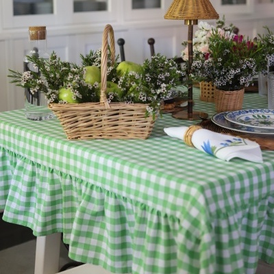 Mesa com toalha xadrez verde e branca e cesta de vime com maçãs e flores