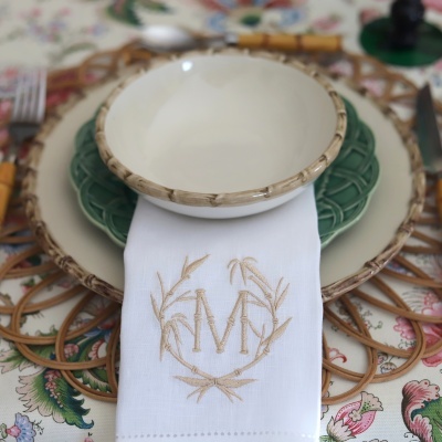 Conjunto de pratos e taça com acabamento em bambu e guardanapo bordado sobre toalha estampada