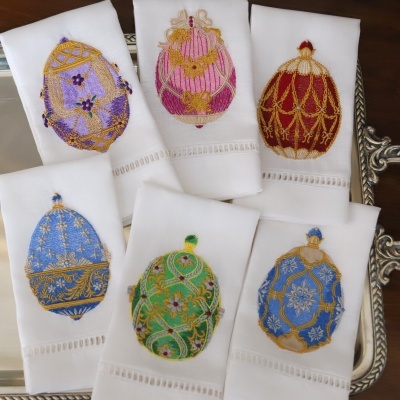 Paninhos brancos com bordados de ovos decorativos coloridos sobre bandeja prateada.