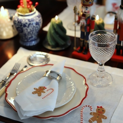 Mesa posta com tema natalício com pratos, guardanapo bordado, copo de vidro e velas decorativas