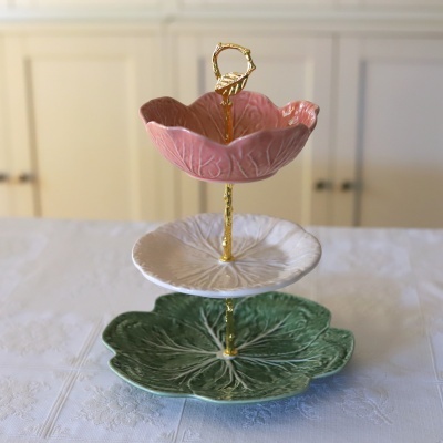 Suporte de três andares em cerâmica com pratos verde, branco e rosa e estrutura dourada.
