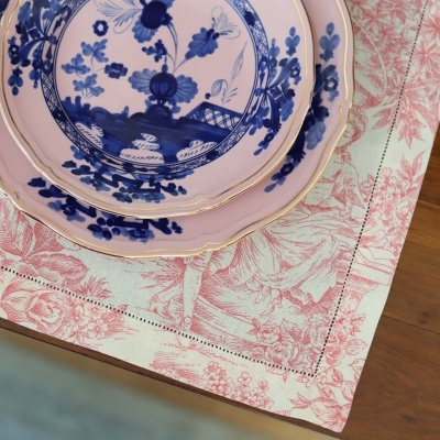 Pratos rosa com flores azuis em pano de mesa branco com padrão vermelho