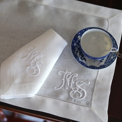 Guardanapo e toalha de linho branco com monograma, chávena e pires azul e branco