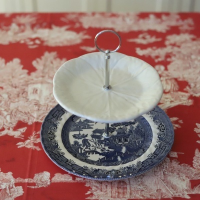 Prato de cerâmica para bolos de duas camadas com padrão azul e branco e suporte metálico prateado.