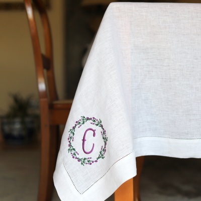 Toalha de mesa branca com bordado floral roxo e verde da letra C no canto
