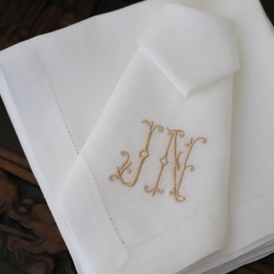 Guardanapos brancos com bordado monograma JM em bege sobre mesa de madeira escura