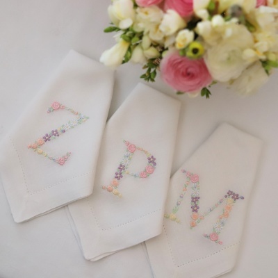 Guardanapos brancos com letras bordadas coloridas e arranjo floral