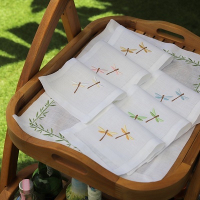 Guardanapos brancos com bordados de libélulas coloridas numa bandeja de madeira