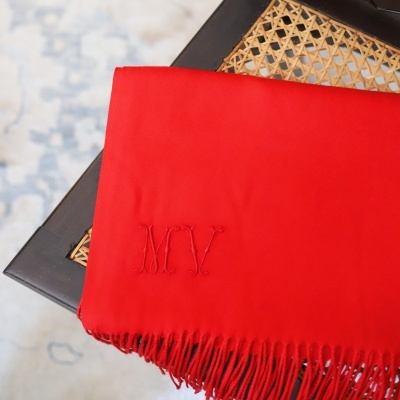 Lenço vermelho com franjas e bordado MCV sobre superfície de madeira e vime