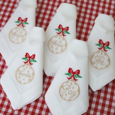 Guardanapos brancos com bordados natalícios coloridos sobre toalha xadrez vermelha e branca