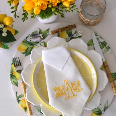 Mesa posta com pratos decorativos de limão, guardanapo bordado branco e talheres com cabos de madeira