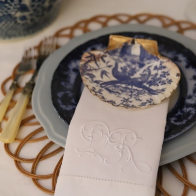 Conjunto de pratos decorados com guardanapo branco monogramado e marcador de lugar em porcelana azul e branca com padrão de ave.