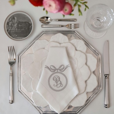 Mesa posta elegante com pratos brancos e metal, guardanapo bordado e talheres