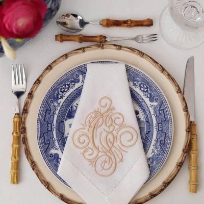 Talheres com cabos de bambu, prato azul e branco, prato suporte imitando madeira, guardanapo branco bordado e toalha branca