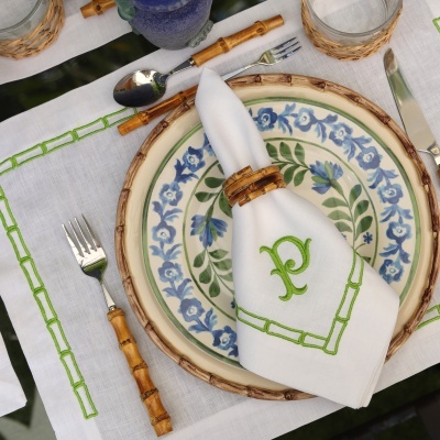 Conjunto de mesa com prato cerâmico azul e verde, guardanapo branco bordado P verde, talheres com cabos de bambu e toalha branca bordada verde.