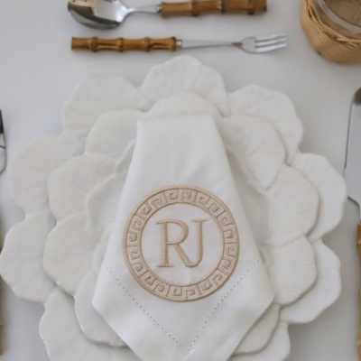 Guardanapo branco bordado RJ sobre prato branco decorativo em forma de pétalas