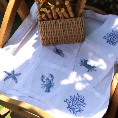 Toalha branca com bordados azuis de temas marinhos numa cadeira de madeira com cesta de vime