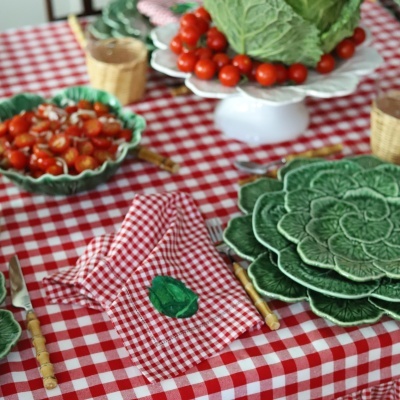 Mesa de jantar com toalha xadrez vermelha, pratos e tigelas verdes com tomates e repolho