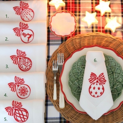Toalhetes de Natal com bordados vermelhos sobre mesa posta com pratos e luzes em forma de estrela